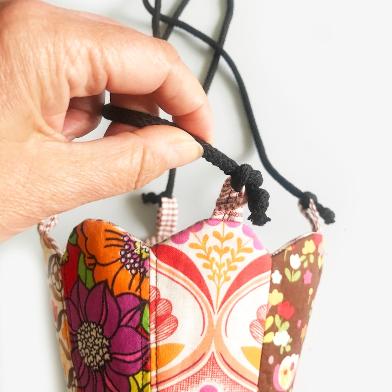 Peut inclure: Une pochette en tissu color&eacute; avec une fermeture &agrave; cordon noir. La pochette est faite de tissu patchwork avec un motif floral.