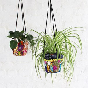 Peut inclure: Deux suspensions pour plantes avec des housses en tissu color&eacute;. La suspension de gauche a un motif floral dans des tons de rose, orange et jaune. La suspension de droite a un motif &agrave; pois bleus et blancs avec une bordure florale jaune et verte.
