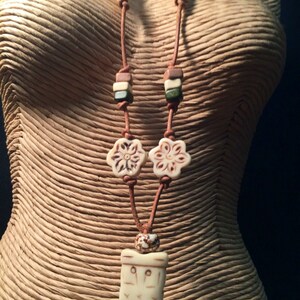 May include: A brown leather necklace with white bone beads, including two flower-shaped beads and a rectangular pendant with a carved design.