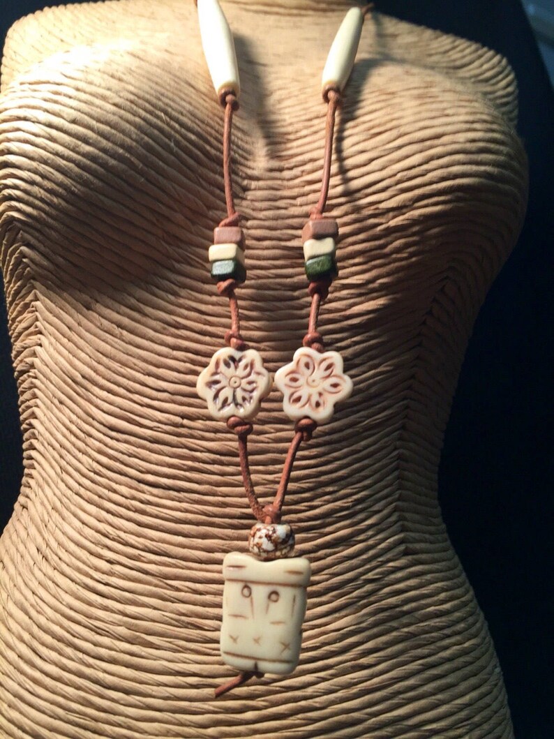 May include: A brown leather necklace with white bone beads, including two flower-shaped beads and a rectangular pendant with a carved design.