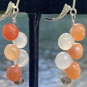 Puede incluir: Un par de pendientes colgantes de plata con una cascada de cuentas de piedras preciosas facetadas de color melocotón, blanco y marrón.