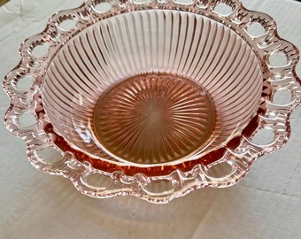 Pode incluir: Uma tigela de vidro rosa vintage com borda ondulada e interior canelado. A tigela tem um design delicado e vazado ao redor da borda. A tigela é provavelmente usada para servir ou exibir.