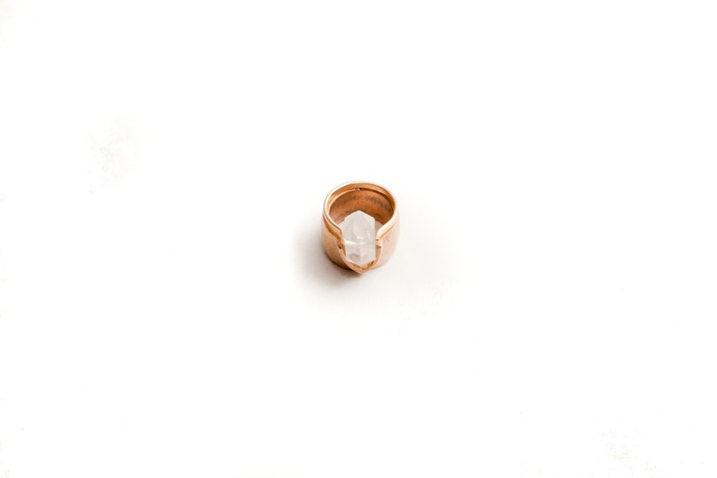 May include: A gold ring with a clear quartz crystal set in the center. The ring is open on one side and the crystal is visible from both sides.