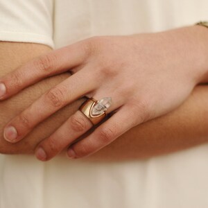 May include: A gold ring with a clear quartz crystal point set in a gold band. The ring is worn on the index finger of a person's hand.