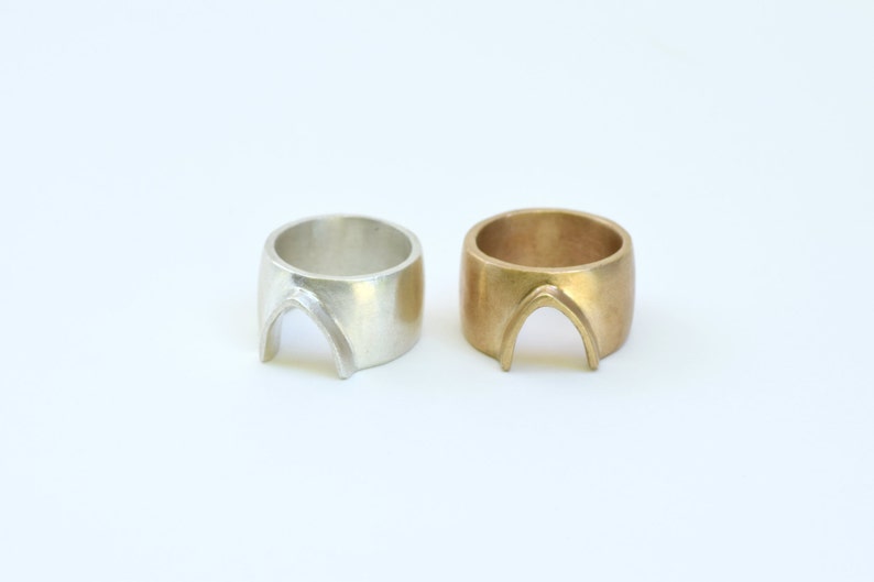 May include: Two rings, one silver and one gold, with an arch-shaped design. The rings are both wide and have a smooth, polished finish.