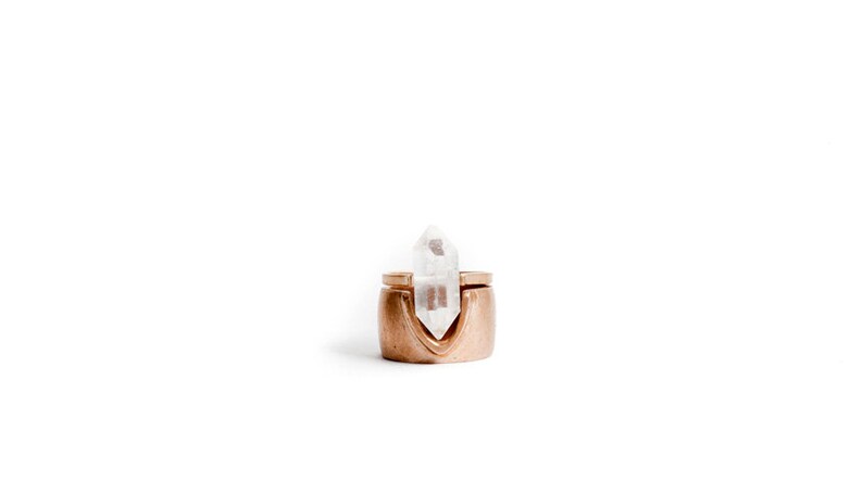 May include: A gold ring with a clear quartz crystal set in the center. The ring is designed to hold the crystal in place.