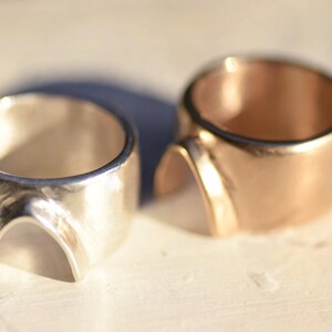 May include: Two rings, one silver and one gold, with a unique arch design. The rings are thick and have a smooth, polished finish.