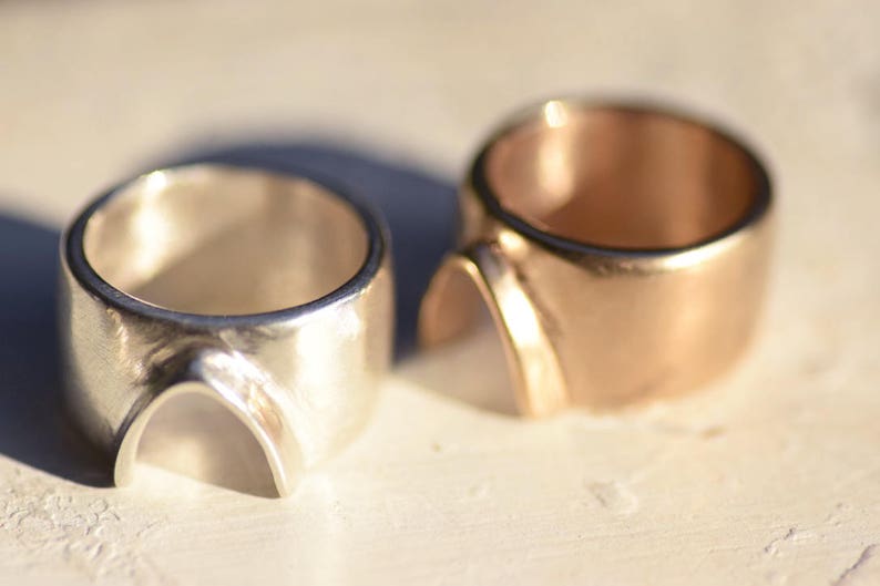 May include: Two rings, one silver and one gold, with a unique arch design. The rings are thick and have a smooth, polished finish.