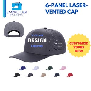 Puede incluir: Una gorra de 6 paneles ventilada con láser con tejido gris y visera negra. La gorra tiene un diseño que dice "YOUR DESIGN HERE" en texto azul. La gorra está disponible en una variedad de colores, incluyendo negro, blanco, rojo, azul, verde y rosa.