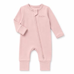 May include: A long-sleeved, dusty pink baby romper featuring a diagonal zipper closure that extends from the neckline to the ankle. The name EMMA is embroidered in a matching pink thread on the upper left chest area of the garment.