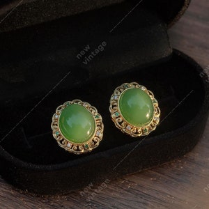May include: A pair of green gemstone earrings with gold settings in a black velvet jewelry box.