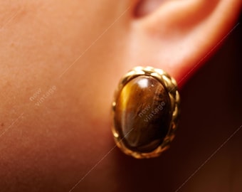 May include: A close-up of a person's ear with a gold earring featuring a brown tiger's eye stone.