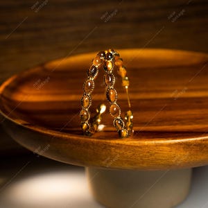 May include: A gold-toned bracelet with oval-shaped tiger's eye stones. The bracelet is displayed on a wooden pedestal with a round top. The background is a warm, neutral tone.
