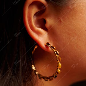 May include: Gold-toned hoop earrings with a series of small, amber-colored stones. The earrings are worn on an ear, with the skin tone visible. The earrings have a vintage aesthetic.