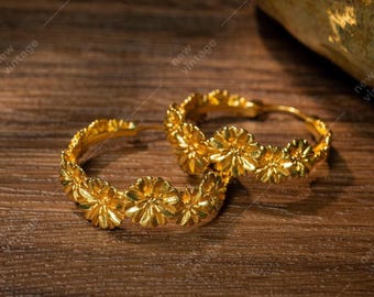 May include: A pair of gold hoop earrings with a floral design. The earrings are made of metal and have a shiny finish.
