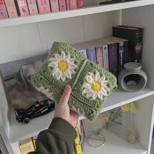 rocheted book cover featuring daisy granny squares with white petals and yellow centres set against a green background. Handmade, floral, and cozy book protection