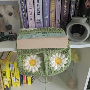 rocheted book cover featuring daisy granny squares with white petals and yellow centres set against a green background. Handmade, floral, and cozy book protection