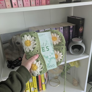 rocheted book cover featuring daisy granny squares with white petals and yellow centres set against a green background. Handmade, floral, and cozy book protection
