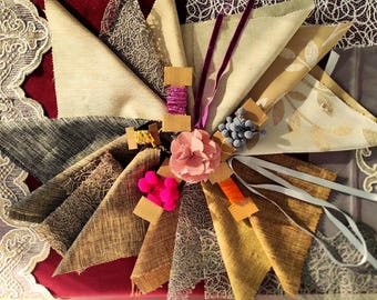 May include: A collection of fabric swatches in various textures and colors, arranged in a fan shape. Includes beige, gray, and brown fabrics, lace trim, and decorative elements like a pink flower, ribbons, and spools of thread. A creative display for textile inspiration.