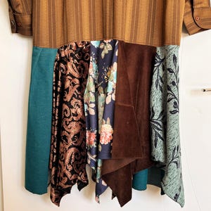 May include: A long-sleeved dress featuring a brown striped upper section and a multi-paneled skirt. The skirt includes panels of solid teal, black fabric with a copper paisley print, a dark blue floral pattern, solid brown suede, and light blue leaf print.