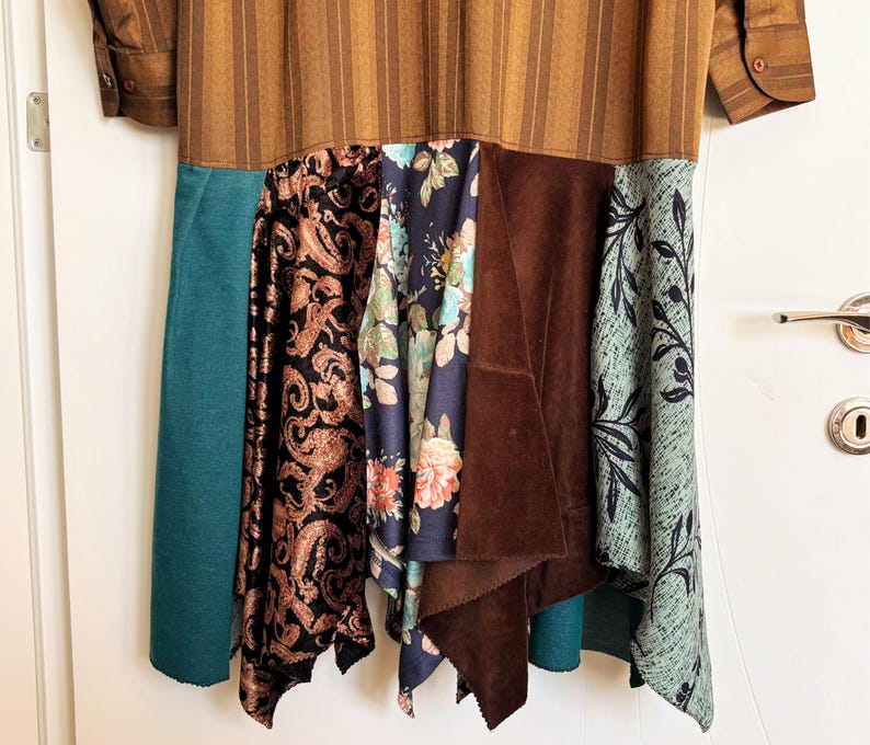 May include: A long-sleeved dress featuring a brown striped upper section and a multi-paneled skirt. The skirt includes panels of solid teal, black fabric with a copper paisley print, a dark blue floral pattern, solid brown suede, and light blue leaf print.