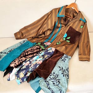 May include: A brown striped button-down shirt featuring a teal collar, a dark brown chest pocket with floral embroidery, and a multi-layered skirt section composed of various fabrics including teal, black, floral, and brown velvet panels.