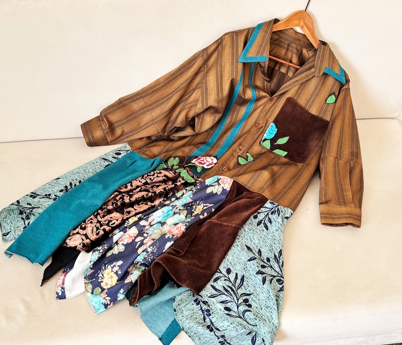 May include: A brown striped button-down shirt featuring a teal collar, a dark brown chest pocket with floral embroidery, and a multi-layered skirt section composed of various fabrics including teal, black, floral, and brown velvet panels.