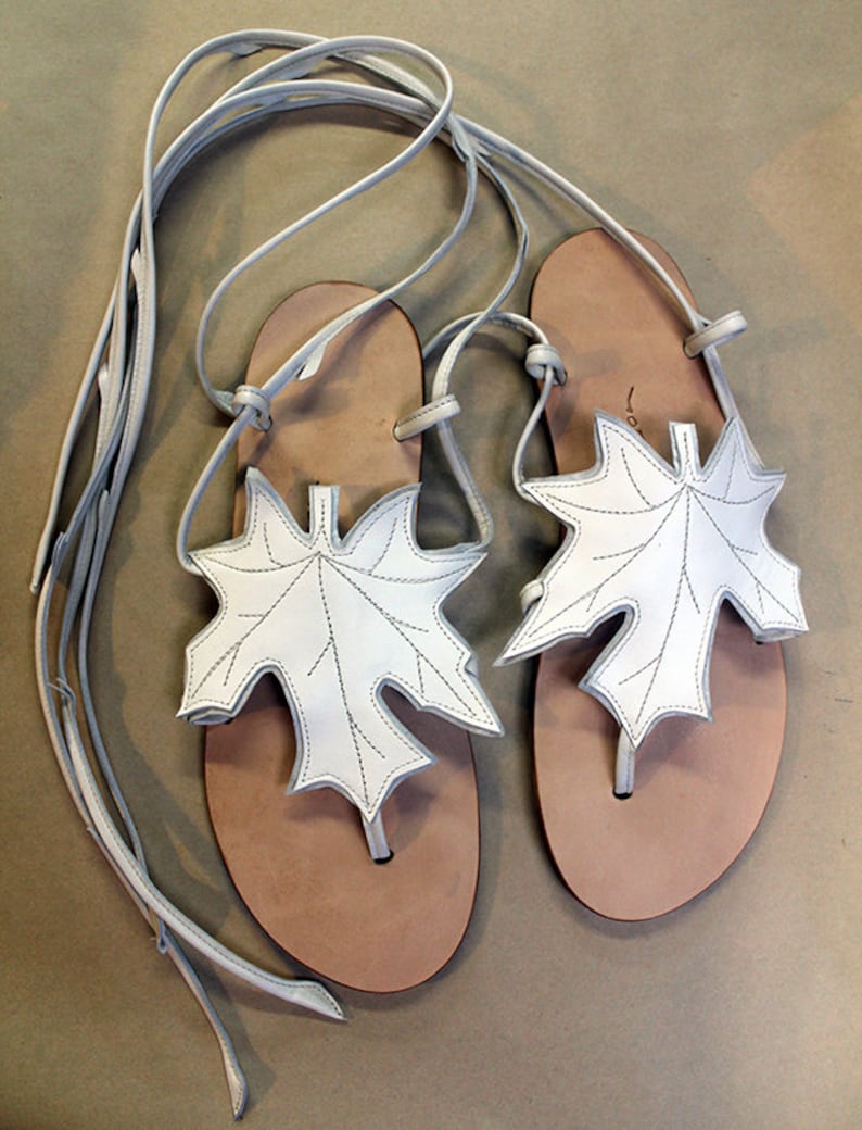 May include: White leather sandals with a leaf design and long laces. The sandals have a brown leather sole.
