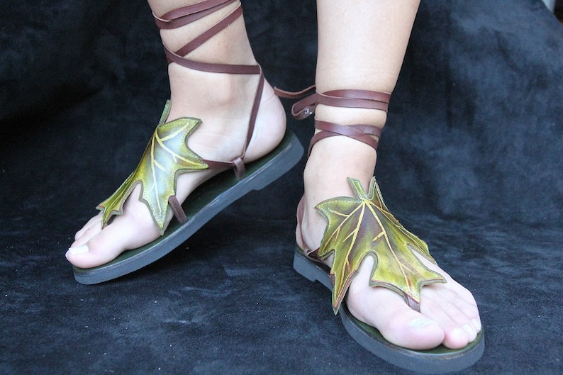 May include: A pair of brown leather sandals with green leaf accents. The sandals have laces that tie up the ankles.