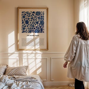 May include: A framed print with a blue and white floral pattern and the text "The Nicene Creed" in a gold frame hanging on a wall in a bedroom. The bedroom has a bed with white and beige bedding and a window with white curtains.