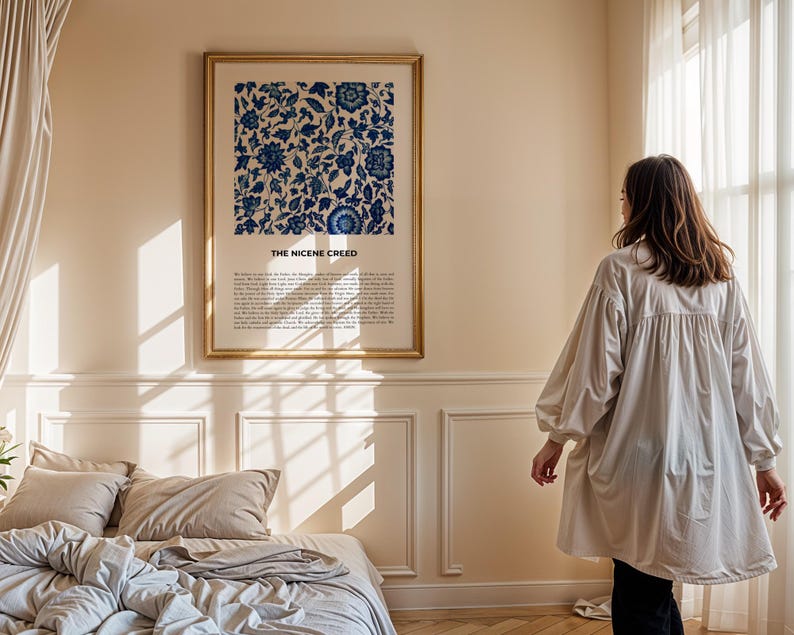 May include: A framed print with a blue and white floral pattern and the text "The Nicene Creed" in a gold frame hanging on a wall in a bedroom. The bedroom has a bed with white and beige bedding and a window with white curtains.