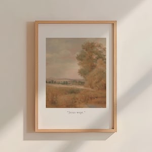 May include: A framed landscape print with a muted color palette. The artwork depicts a field, trees, and a cloudy sky. The text "Jesus wept." is printed at the bottom of the image. The frame is made of light-colored wood.