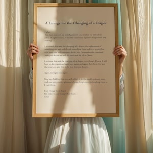 May include: A framed print with a white background and black text. The text reads "A Liturgy for the Changing of a Diaper." The text is a poem about the act of changing a diaper and the love and forgiveness that comes with it.