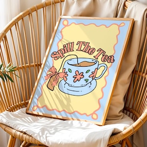 Puede incluir: Un cuadro enmarcado con la ilustración de una taza de té y el texto "Spill The Tea". La taza es azul claro con detalles florales y una bolsita de té. El fondo es amarillo con un borde azul claro, todo en un marco de madera.