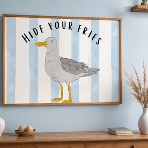 Könnte beinhalten: Ein gerahmter Kunstdruck mit einer Cartoon-Illustration einer Möwe. Die Möwe ist grau mit gelben Beinen und einem gelben Schnabel, vor einem blau-weiß gestreiften Hintergrund. Der Text "HIDE YOUR FRIES" steht in Schwarz über der Möwe.