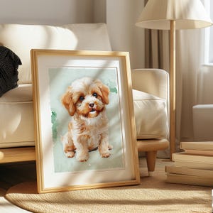 May include: A framed watercolour print of a small, fluffy puppy with tan and white fur. The puppy is sitting on a light green background with green watercolour accents. The frame is made of light-coloured wood, displayed on a rug.