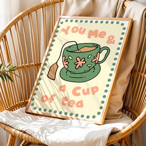 May include: A framed print featuring a green teacup with pink floral accents and a tea bag. The text "You me & a cup of tea" is written in a playful font. The artwork is set against a light yellow background with a dotted border.