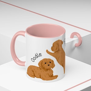 May include: A pink and white ceramic mug with a brown doodle dog illustration. The mug has the word "Doodle" written on it.
