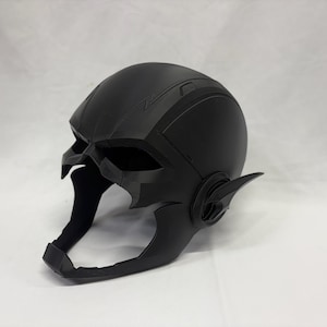 Könnte beinhalten: Ein mattschwarzer Helm mit stilisiertem Design, Blitzsymbol auf der Stirn und flügelförmigen Vorsprüngen an den Seiten. Der Helm hat eine futuristische Ästhetik, wahrscheinlich für Cosplay oder zur Präsentation.