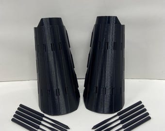 May include: Two black, cone-shaped objects with vertical lines and rectangular cutouts, accompanied by two sets of five black, pointed rods. The items are arranged on a white surface, suggesting a set or collection of tools or components.