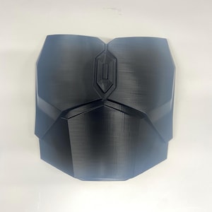 May include: A black 3D printed chest piece with a geometric design. The chest piece has a raised, rectangular panel in the centre.