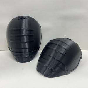 Puede incluir: Dos rodilleras negras impresas en 3D con una superficie texturizada.
