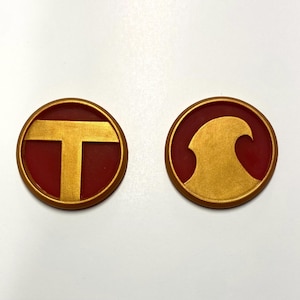 May include: Two round, red, and gold badges. The first badge has a gold "T" on a red background. The second badge has a gold wave on a red background.