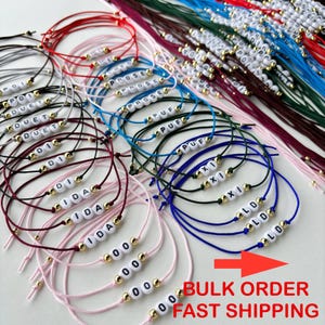 May include: A selection of vibrant string bracelets, each with white letter beads forming words and names. The bracelets are adorned with gold-toned beads and are displayed on a white background. The image also includes the text "BULK ORDER FAST SHIPPING".