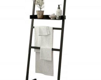 May include: Black metal towel ladder with a shelf and two towel bars. The ladder has a small plant and a bottle of lotion on the shelf.