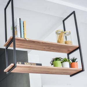 Könnte beinhalten: Ein schwarzes Metallregal mit zwei Holzböden. In dem oberen Regal stehen Bücher und zwei Glasbehälter mit Pasta. Im unteren Regal liegt ein Buch mit dem Titel "1000 Drinkow" und drei Topfpflanzen.