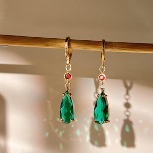 May include: A pair of gold dangle earrings with green teardrop-shaped crystals and small red accent stones.