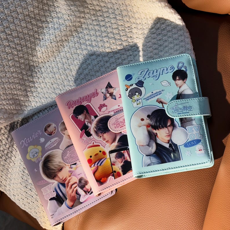 May include: Three faux leather journals in lavender, pink, and light blue, each with a magnetic closure. The journals feature images of a person and cartoon characters, and the names 'Xavier', 'Rasayel', and 'Zayne'.