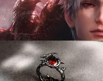 May include: A black ring with a large, oval, red gemstone. The ring has a detailed, nature-inspired design with a bird and branch motif. The background features a digital illustration of a raven and a person with red eyes.
