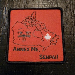 Puede incluir: Un parche cuadrado bordado con fondo rojo y borde negro. Presenta un mapa de contorno negro de Canadá con ojos de estilo anime y una boca sonrojada, una hoja de arce blanca y el texto negro "ANNEX ME, SENPAI!" impreso en la parte inferior.